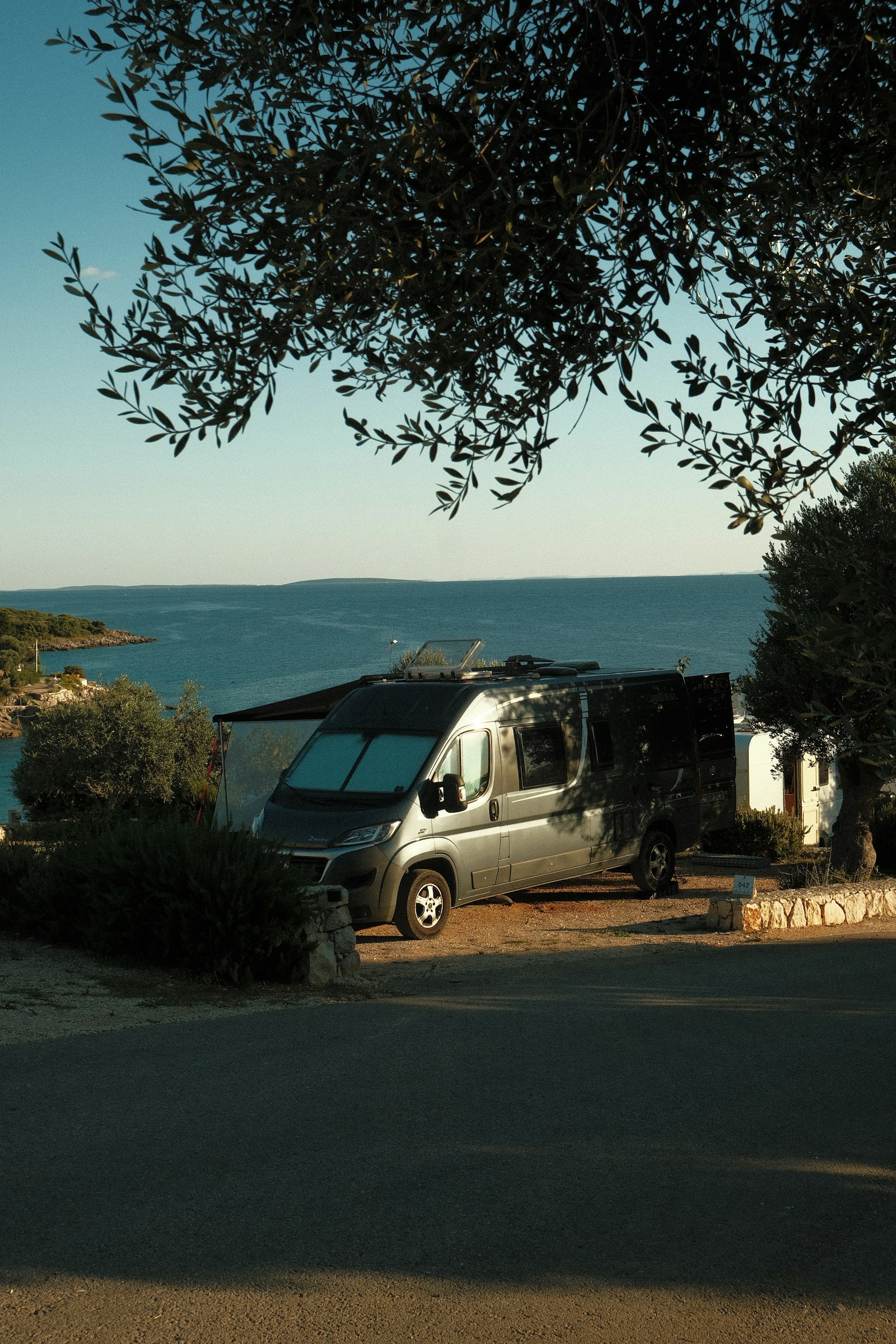 Campervan am Meer unter Bäumen